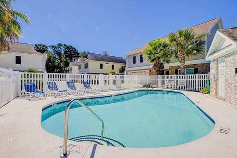 Inviting pool with lounge chairs, palm trees, and a white picket fence.








