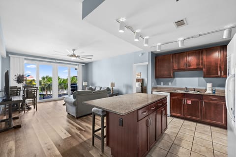 Step into your bright, open-concept retreat where rich wood cabinetry meets coastal views. The spacious kitchen island invites morning coffee while palm trees sway beyond your private balcony.