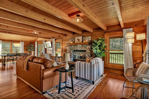 Gorgeous log cabin with fireplace, open concept living and dining spaces, TV, dining room table with space for 6, and plenty of seating.