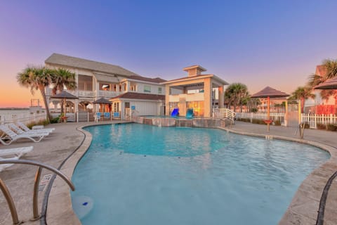 Modern beachfront property with sparkling pool area featuring tropical palm trees and stunning sunset views over the coastal landscape.