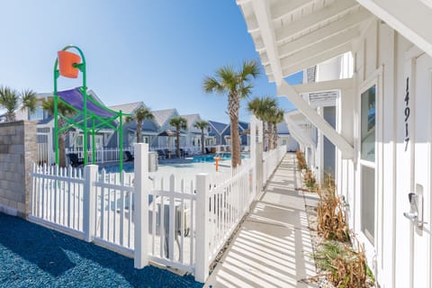 Coastal vacation rental community with kids' playground, pool, and palm-lined walkways under sunny skies.