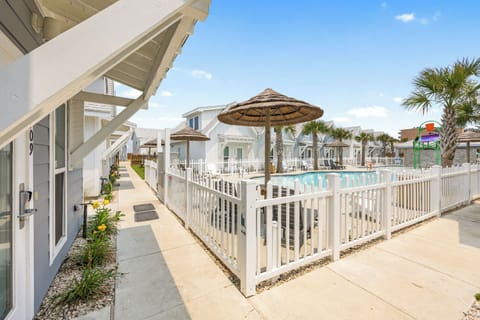 Modern coastal resort community with swimming pool, tropical landscaping, and beach-style accommodations under sunny skies.