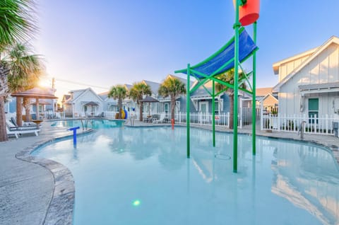 Family-friendly aqua park with water slides and splash features surrounded by charming beach cottages and palm trees.