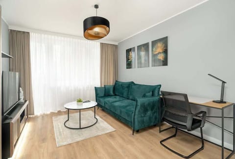 A modern living room with a green velvet armchair, grey sofa, minimalist coffee table, and large windows with sheer curtains, maintaining a bright and elegant atmosphere.
