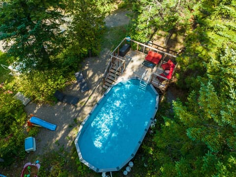 Vue aérienne de la piscine entourée de forêt et d’un coin détente sur terrasse.