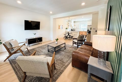 LIVING ROOM– This spacious and ope n living area seamlessly connects to the dining and kitchen spaces, creating a welcoming environment perfect for relaxation or entertaining. The comfortable seating arrangement, complete with a cozy leather sofa and stylish accent chairs, faces a mounted flat-screen TV for a perfect movie night or catching up on your favorite shows. The soft l...