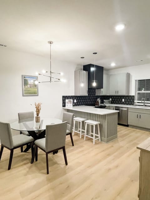 KITCHEN - This kitchen and dining area features a modern design with a sleek, stylish lighting fixture above the table, providing an inviting space for meals and gatherings. The island offers additional seating and counter space, perfect for casual dining or food preparation. The open layout is ideal for hosting and enjoying time together.