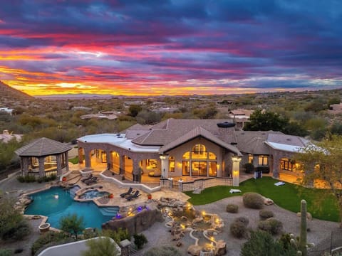 A luxurious desert estate framed by a vibrant sunset, featuring an expansive pool, outdoor entertaining spaces, and stunning natural surroundings.