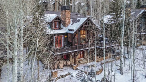 Charming mountain cabin nestled among snow-covered aspens with stone chimney and warm glowing windows in winter wonderland.