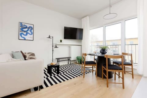 Bright living area with a beige sofa, black-and-white striped rug, and a small dining table near the window.
