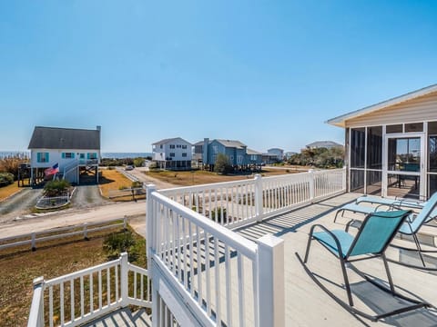 Spacious upper deck with lounge chairs, white railing, and ocean views, overlooking nearby coastal homes and screened porch—perfect for relaxing in the sun at this Oak Island beach retreat.