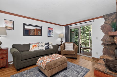 Unwind in your cozy living room with plush seating, charming stone fireplace, and peaceful forest views from your private balcony.