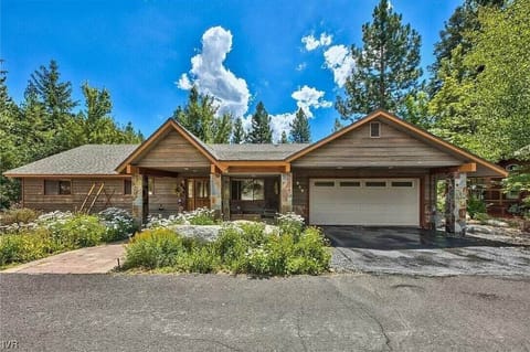 Cabin exterior with front porch, walkway, driveway, shrubs, and trees.