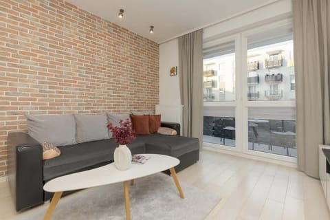 Stylish living room with an exposed brick accent wall, a cozy gray sofa, and large floor-to-ceiling windows.
