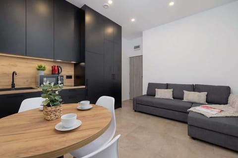 A stylish, modern kitchen with dark matte cabinets, a wooden countertop, and a cozy dining setup, creating a sleek yet inviting atmosphere.
