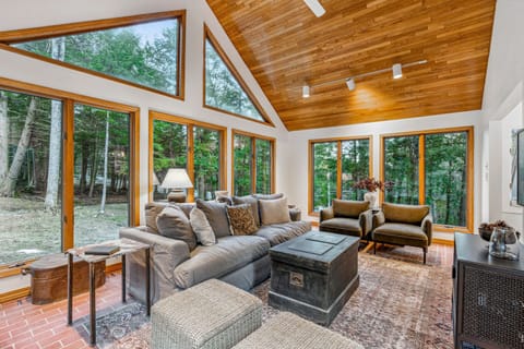 Sunroom living area with sectional sofa, velvet chairs, and forest views