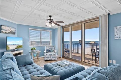 - Oceanfront living room with floor-to-ceiling glass doors   - Blue sectional and TV for relaxing after sunny beach days   - Step onto balcony for sea breeze and sparkling views
