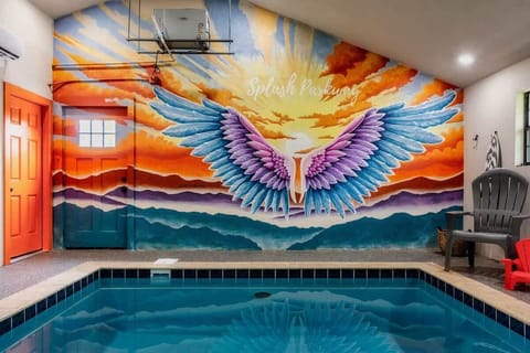 Indoor pool area featuring a vibrant mural of colorful wings against a sunset backdrop.