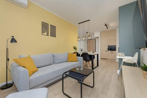 Living room with a light blue sofa, a coffee table, and large artwork on the wall, featuring a yellow accent wall and large windows.