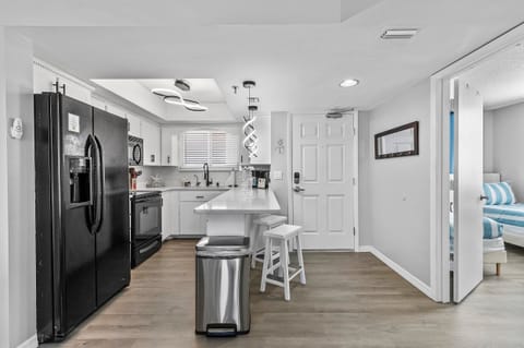 his sleek, modern kitchen showcases a clean design with white cabinetry, a black refrigerator, and matching black appliances. The open layout features a central island with bar seating, perfect for casual dining or morning coffee.