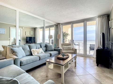 This airy living room features plush seating, a coffee table, and expansive windows offering stunning ocean views. The comfortable and inviting atmosphere is perfect for relaxing or watching TV after a day at the beach.