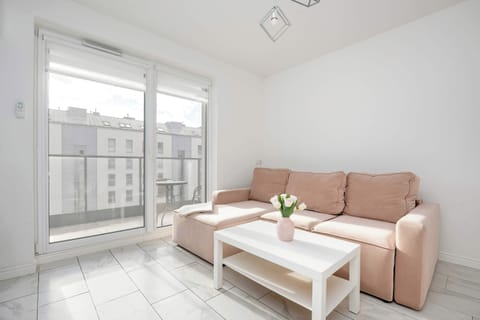A bright living room with a soft pink sofa, a white coffee table, and large windows leading to a balcony.
