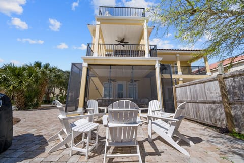 Beautiful three-story beach house with spacious patio featuring classic white Adirondack chairs for relaxing under tropical palms.