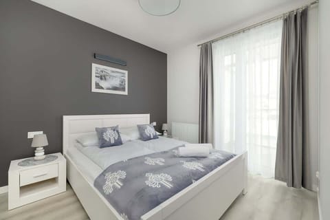 A stylish bedroom with a gray upholstered bed, white bedside tables, and floor-length curtains.

