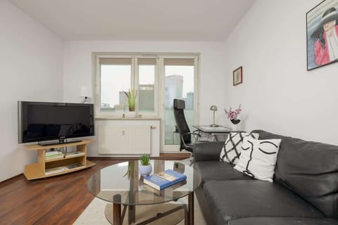 A cozy living room with a black leather sofa, a TV, and a work desk, offering a functional and comfortable space.

