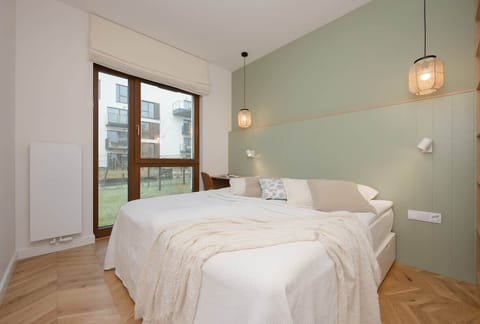A stylish bedroom with a large bed, warm lighting, and a sliding glass door leading to a balcony, creating a cozy and inviting atmosphere.


