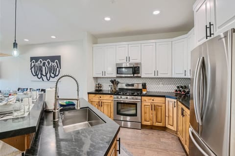 Prepare meals in the fully equipped kitchen, featuring a large island with sink, black granite countertops, and modern stainless steel appliances including a microwave and range.