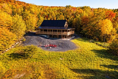 Large cabin surrounded by vibrant fall foliage with a wraparound deck, fire pit, and scenic mountain views.