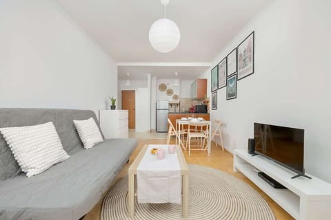 A bright and modern living room with a gray sofa, white TV stand, and a cozy rug, complemented by framed artwork on the walls and a dining area in the background.

