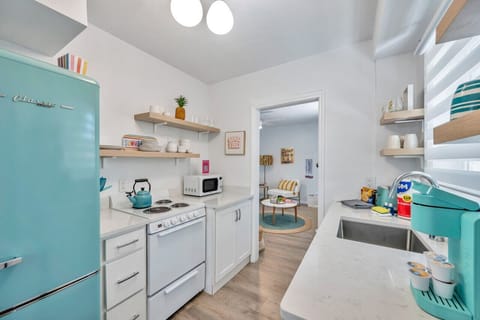 Bright kitchen view w/ open shelving, teal accents, & a clean, airy layout.