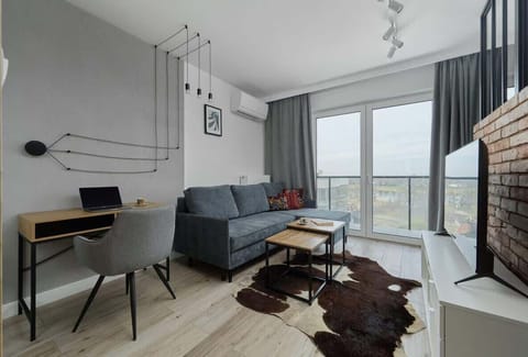 A stylish living area with a modern sofa, a workspace with a desk and chair, and large windows that allow natural light to flood the space.

