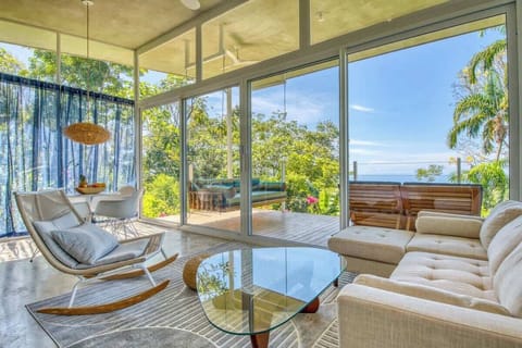 Airy living room with A/C, Wi-Fi, and floor-to-ceiling glass walls overlooking the jungle and ocean. Relax on modern lounge seating or step onto your private terrace for seamless indoor/outdoor living in Dominical