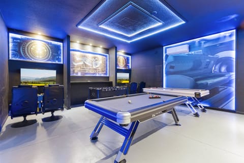 Experience the lively game room with a sleek air hockey table, promising endless fun. The modern design, accented by blue LED lighting and eye-catching wall art, sets a vibrant atmosphere ideal for gatherings and relaxation.