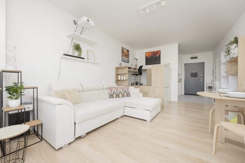 A bright and spacious living room with a white sofa, modern decor, and open shelving, creating a cozy and inviting atmosphere.

