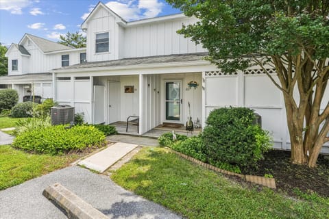 A charming two-story vacation rental featuring classic white siding and green landscaping, offering a welcoming arrival experience in a peaceful neighborhood setting.