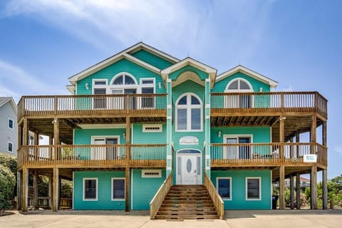Welcoming turquoise beach house with spacious wraparound decks on multiple levels, offering ample outdoor space and a bright coastal charm.