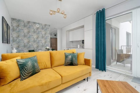 A stylish living area with a mustard yellow sofa, decorative green pillows, and an accent wall with patterned wallpaper.

