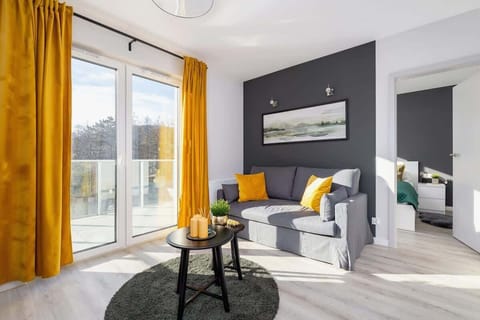 A modern living room with a dark accent wall, a gray sofa, mustard yellow curtains, and a round coffee table, creating a stylish and cozy atmosphere.

