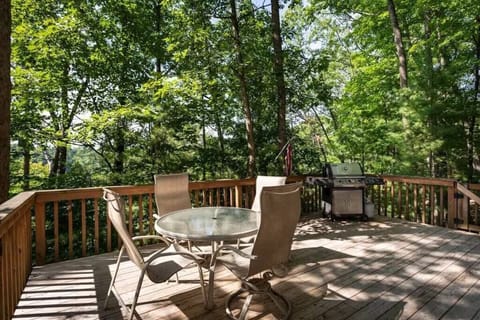 Spacious back deck w/ grill & patio seating, surrounded by trees for relaxed outdoor dining.