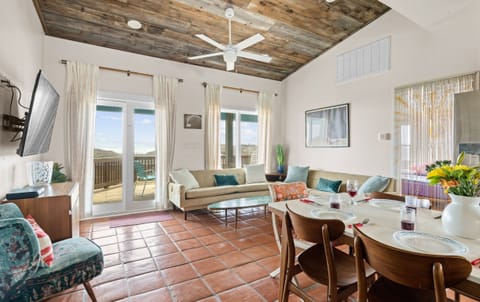 Living Room — Tan Sofa, Teal Pillows, Wall TV, Reclaimed Wood Ceiling, Sheer Curtains & Deck View