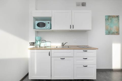 A compact yet fully equipped kitchen with sleek white cabinetry, a modern countertop, and pastel-colored kitchen appliances that enhance its stylish design.