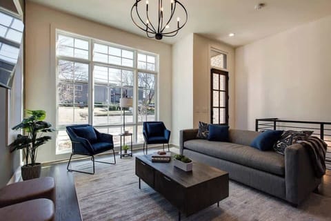 Sun-drenched living room with a gray couch, two blue chairs, and expansive windows.