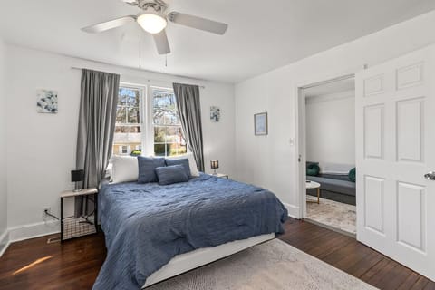 Experience comfort and functionality in our cozy bedroom, featuring a queen bed, workspace, ceiling fan, blackout curtains, and ample clothing storage for your convenience.