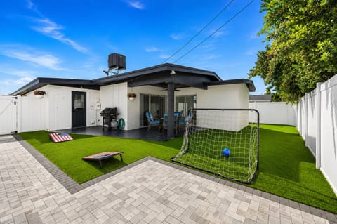 Wide-angle backyard view featuring outdoor games, covered patio, and open green space.