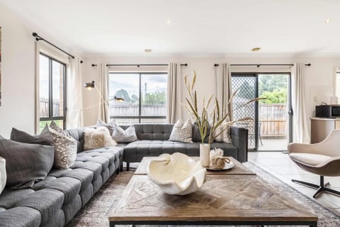 LIVING AREA: Cozy up in the spacious, sunlit living room featuring a plush sectional, soft throws, and large windows overlooking a private backyard