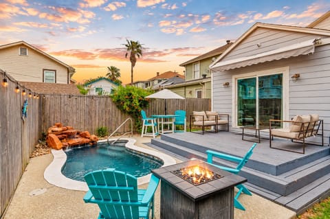 Private backyard pool with entry steps, turquoise Adirondack chairs, raised deck seating and a gas fire pit at this Galveston vacation rental near Avenue Q.